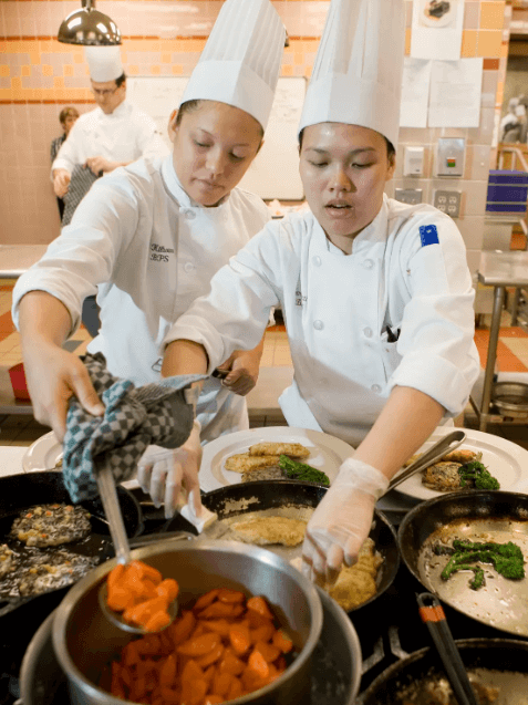 CIA students plate dishes in the kitchen.