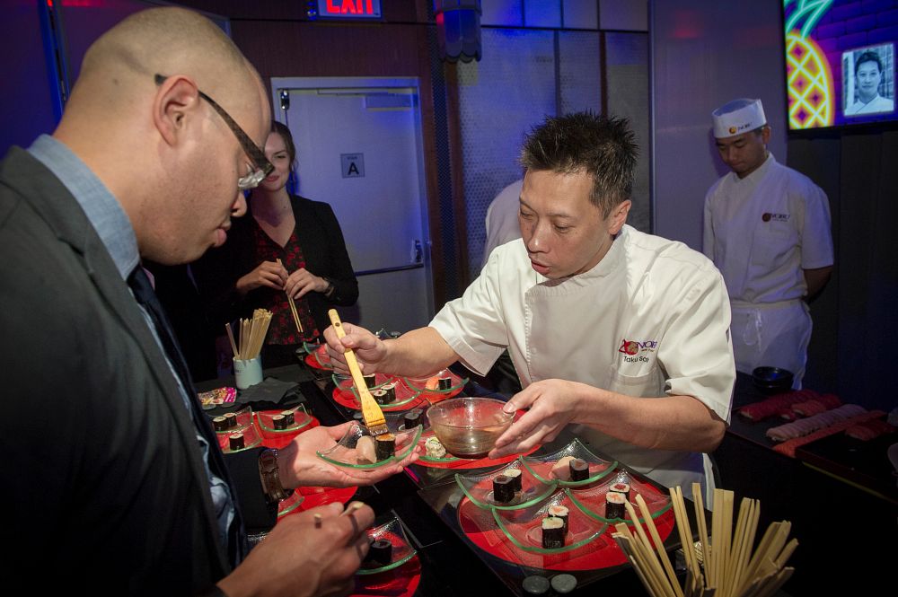 Nobu executive chef Taku Sato presents an appetizer table at the 2019 Masters of Hospitality Leadership Awards at The Ziegfeld Ballroom in New York City. Chef Sato is dressing a guest's maki roll with soy sauce.