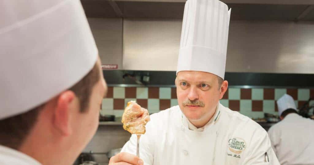 David McCue ’93, CIA Professor of Culinary Arts, showing a student a piece of chicken on a fork.