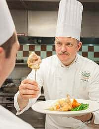 David McCue ’93, CIA Professor of Culinary Arts, showing a student a piece of chicken on a fork.