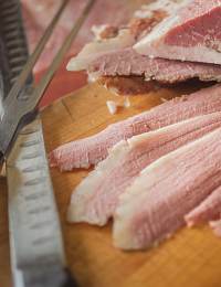 Close-up image of sliced corned beef on a wooden cutting board. There is a sharp knife with a serrated edge next to the slices. The meat appears juicy and marbled with fat, showcasing its tender texture.