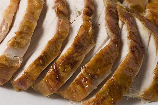 Sliced roasted turkey breast arranged in close layers, showing golden brown, crispy skin on each slice. The meat appears moist and tender, showcasing a well-cooked and appetizing dish.