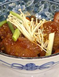 A bowl of braised pork with glossy sauce, garnished with fresh green onions and enoki mushrooms. The bowl has a decorative blue and white floral pattern.