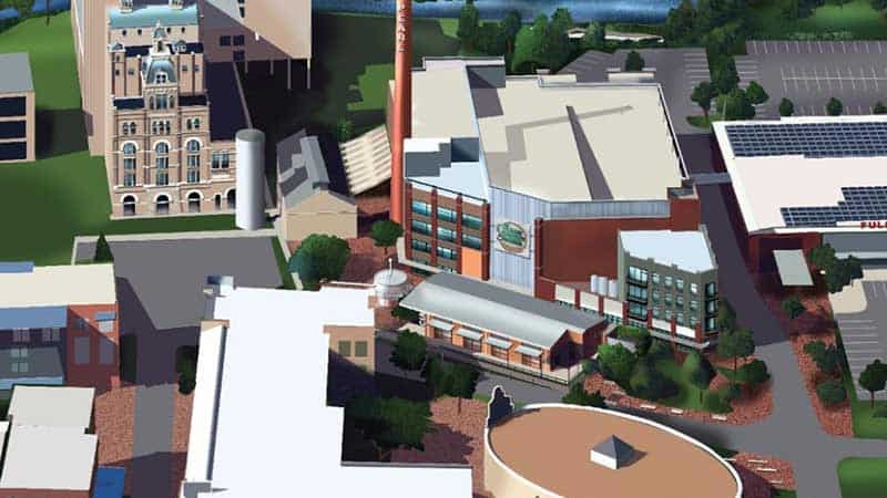 An aerial illustration of a brewery complex featuring multiple buildings. The site includes an iconic smokestack, a circular structure in the foreground, and various industrial and office buildings surrounded by greenery and an adjacent river.