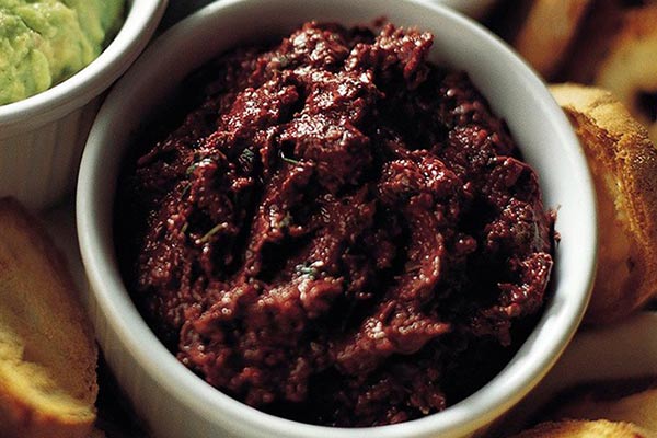 Image of black olives, anchovy fillets, capers, and garlic tapenade in a ramekin.