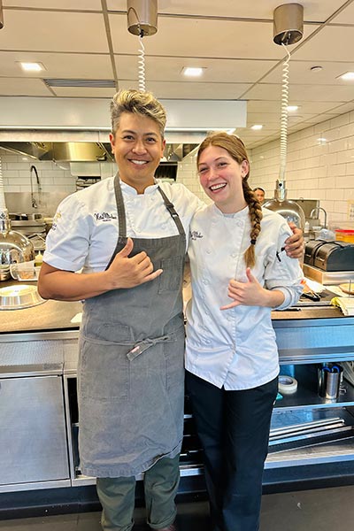 Image of Ella Ackerman standing in a kitchen with a chef.