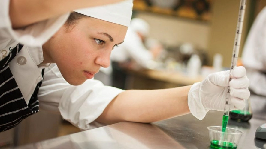CIA Culinary Science Lab with a student measuring a green liquid.