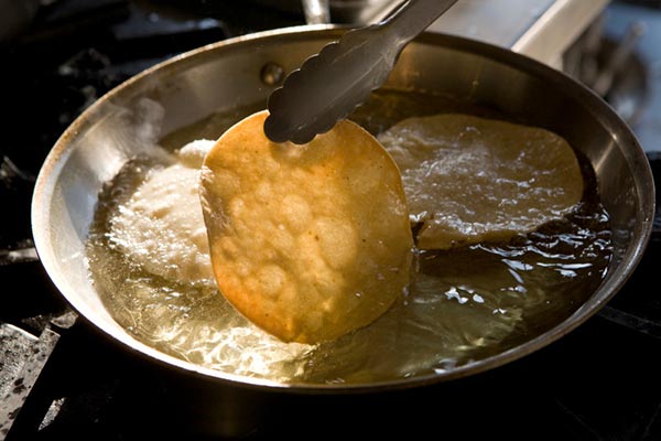 Image of a tortilla chip being fried in a pan with oil.