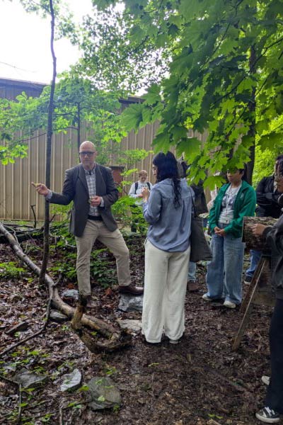 Image of CIA Professor Dr. Taylor Reid talking to students in the woods.