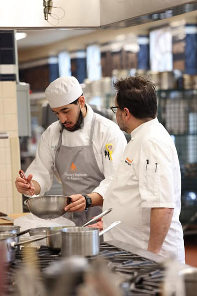 Image of a CIA student in the kitchen with a chef-instructor.