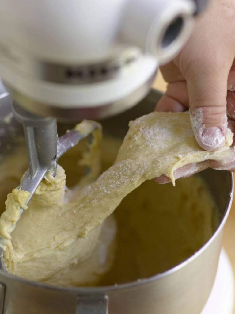 image_tooltip A close-up of artisan bread dough in a mixing bowl. A hand covered in flour pulls at the dough to check the consistency.