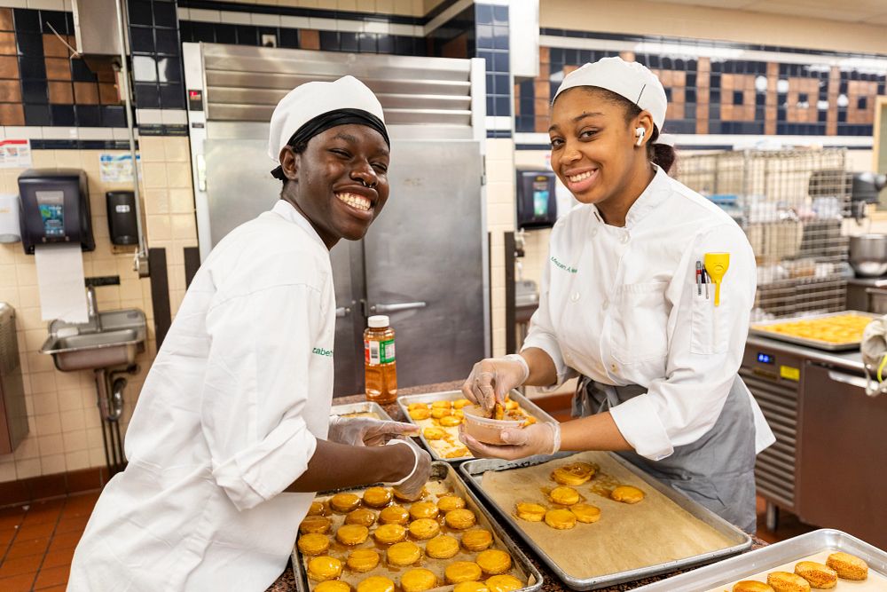 image_tooltip Students smile for the camera as they prepare cornbread for the CIA's Annual Chili Cook-Off Competition.