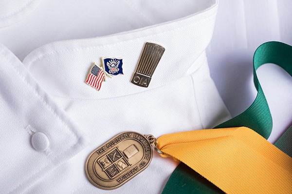 Image of CIA pin and graduation medal on a white chef’s jacket.