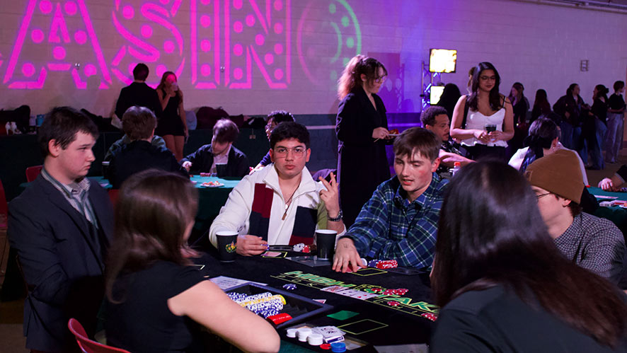 CIA students playing casino table games indoors with chips and drinks under “CASINO” lights.